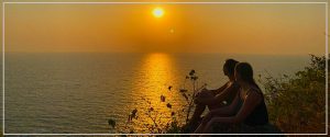 A group of people sitting on a cliff and enjoying sunset at India Yoga School.